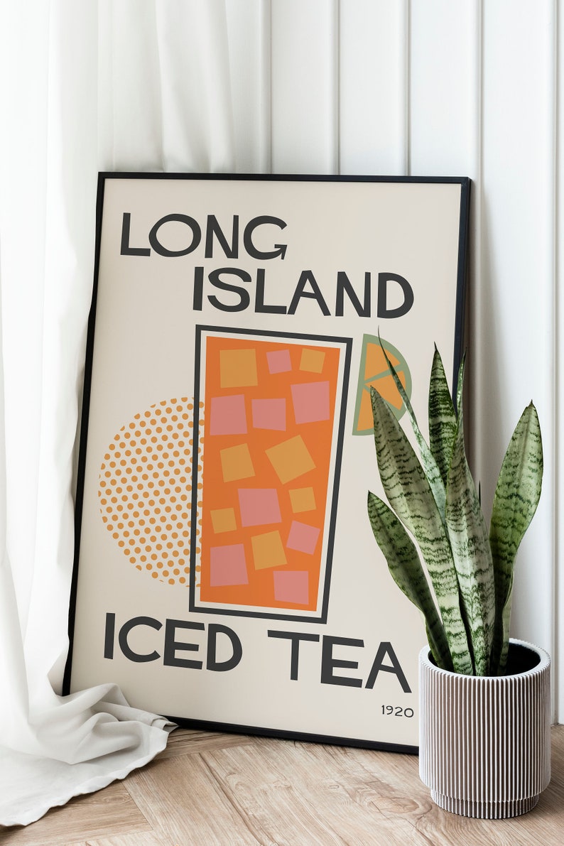 May include: A framed poster with a retro design featuring the text "Long Island Iced Tea" and a stylized illustration of a glass of iced tea. The poster is in a black frame and is leaning against a white wall.