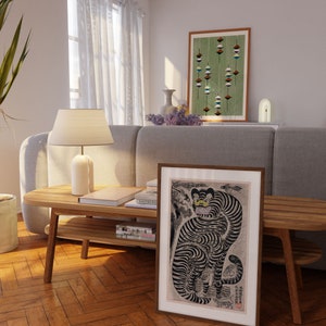 Peut inclure: Une estampe sur bois en noir et blanc d'un tigre avec un motif ray&eacute; d&eacute;taill&eacute;. Le tigre est assis sur un rocher avec un poisson et un serpent en arri&egrave;re-plan. L'estampe est encadr&eacute;e dans un cadre en bois fonc&eacute;.