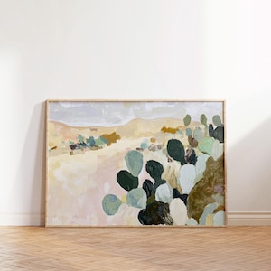 May include: Abstract landscape painting depicting a desert scene with cacti in shades of green, brown, and blue. The artwork is framed in light wood and shows a serene, natural environment with soft, muted colours.