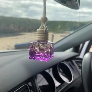 May include: A purple glass car air freshener with a textured design hangs from a rearview mirror. The air freshener is attached to a string with a wooden bead.