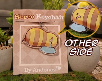 May include: A yellow and brown cartoon bee keychain with a blue puddle underneath. The keychain is on a card that says "Scree Keychain" and "By Andonoz". The other side of the keychain shows the bee crying.