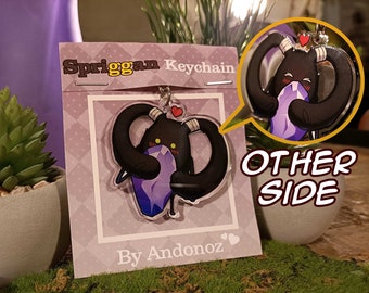 May include: A black and purple Spriggan keychain with a heart on its head. The keychain is holding a purple gem. The text "Spriggan Keychain" and "By Andonoz" are on the card behind the keychain. The text "OTHER SIDE" is on a white speech bubble.