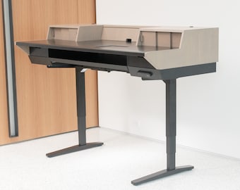 Puede incluir: Un escritorio de pie negro y gris con una tapa de madera y un estante incorporado. El escritorio tiene un panel de control en la parte delantera y dos patas negras.