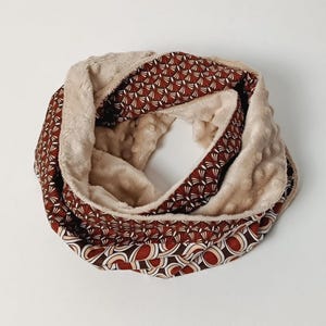 Peut inclure: Écharpe circulaire confortable avec un intérieur beige doux et un extérieur à motifs. L'extérieur présente un motif répétitif dans les tons marron, crème et rouge. Cet accessoire chaud est parfait pour l'hiver.