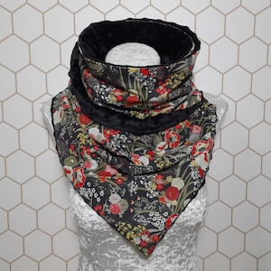 Può includere: Sciarpa a collo floreale nera con fiori rossi, gialli e bianchi. La sciarpa ha una fodera e un bordo in peluche nero. La sciarpa è esposta su un manichino. Lo sfondo è un motivo a piastrelle esagonali bianche.