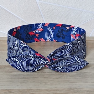 Könnte beinhalten: Ein blaues und weißes Stirnband mit einem Muster aus Wellen und roten Fischen. Das Stirnband ist oben in einem Knoten gebunden.
