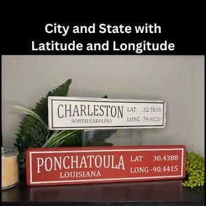May include: Two rectangular signs with city names, state, latitude, and longitude. The top sign reads "Charleston, South Carolina" in black on a white background. The bottom sign reads "Ponchatoula, Louisiana" in white on a red background.
