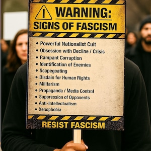 May include: A person holding a sign with a yellow and black warning border. The sign reads "WARNING: SIGNS OF FASCISM" and lists characteristics such as "Powerful Nationalist Cult" and "RESIST FASCISM".