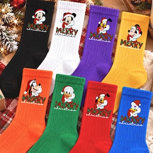 May include: A set of eight ribbed crew socks in black, white, purple, yellow, orange, green, red, and blue. Each sock features a Disney character wearing a Santa hat above the text Merry Christmas in a green and red plaid font pattern.