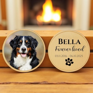 May include: Two round wooden pet memorial ornaments. One features a color photo of a Bernese Mountain Dog. The other has the name "BELLA", the text "Forever loved", dates, and a paw print.