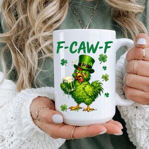 May include: White ceramic mug with the text "F-CAW-F" in green. The mug features a green chicken wearing a green hat and holding a green beer. Shamrock designs are also on the mug.
