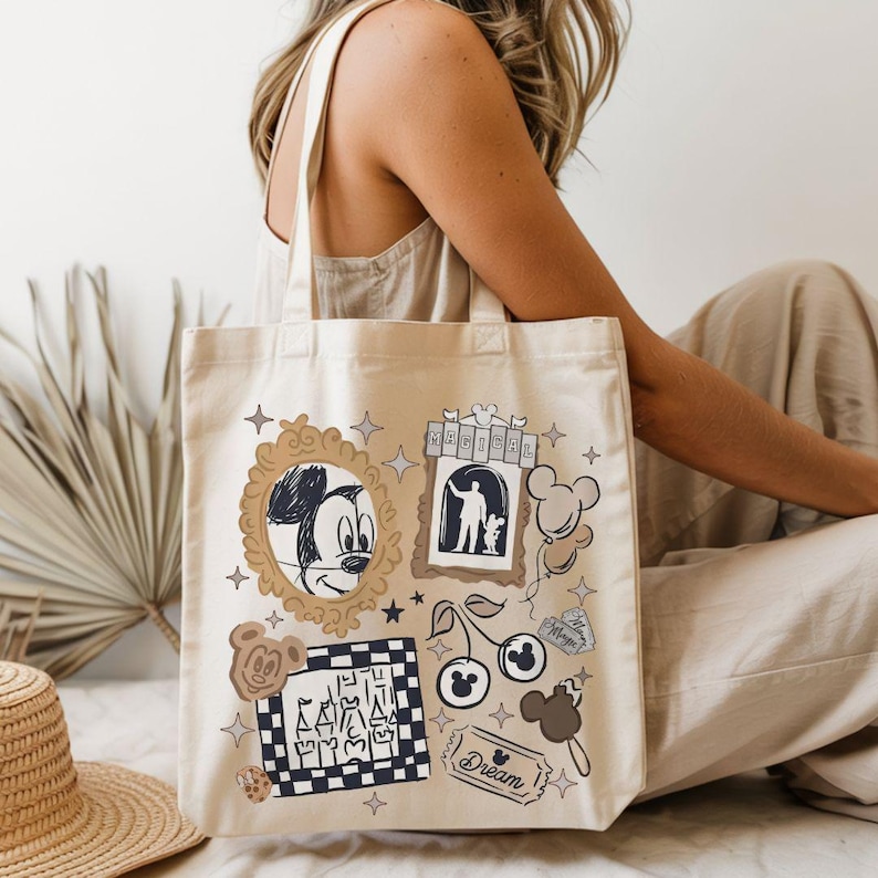 Puede incluir: Bolso tote de lona beige con un collage tem&aacute;tico de Disney. El dise&ntilde;o incluye un boceto de Mickey Mouse, un castillo, cerezas y la palabra "Dream". El bolso tiene dos asas.