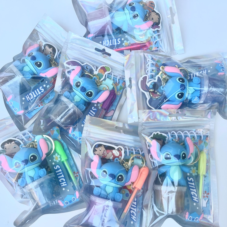 May include: A collection of Stitch character keychains and pens in clear plastic bags. The keychains feature a blue alien with large ears and a pink nose. Some bags include pens with the word "Stitch" printed on them.