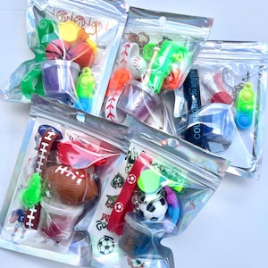 May include: Assorted sports-themed party favors in clear, resealable bags. Each bag contains a variety of items, including mini sports balls, keychains, and colorful fidget toys. The bags are filled with items in red, green, blue, and white.