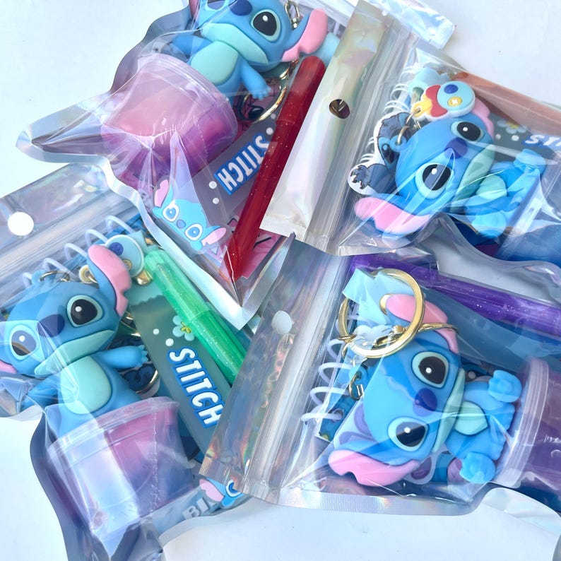 May include: Assortment of Stitch-themed keychains and pens in clear plastic bags. The keychains feature a blue character with pink ears and accents. Some bags contain pens in red and green. The word "STITCH" is visible on some items.