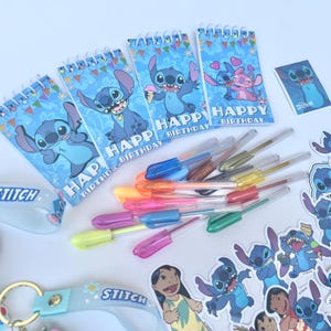 May include: A collection of Stitch-themed stationery and accessories. Includes spiral notebooks with "Happy Birthday" text and Stitch illustrations, colorful gel pens, stickers, and a keychain. The items are arranged on a white surface.