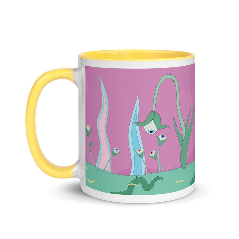May include: A white ceramic mug with a yellow rim and a pink background. The mug features a whimsical illustration of green plants with blue and pink flowers that have eyes.