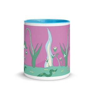 May include: A white ceramic mug with a light blue rim features a whimsical design of green plants with eyes on a pink background. The plants have white flowers with eyes and are surrounded by a green grassy area with a green snake.