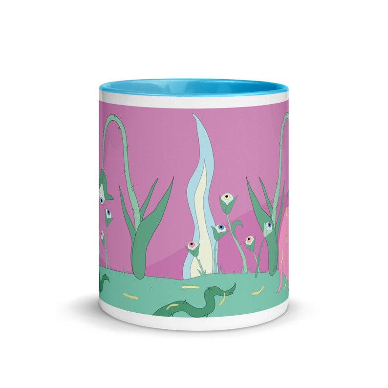 May include: A white ceramic mug with a light blue rim features a whimsical design of green plants with eyes on a pink background. The plants have white flowers with eyes and are surrounded by a green grassy area with a green snake.