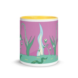 May include: A white ceramic mug with a yellow rim and a pink background. The mug features a whimsical design of green plants with blue and white flowers that have eyes. The flowers are surrounded by a green snake and yellow lines.