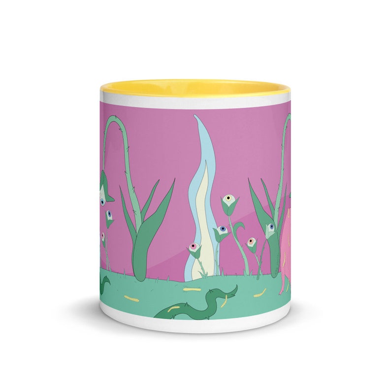 May include: A white ceramic mug with a yellow rim and a pink background. The mug features a whimsical design of green plants with blue and white flowers that have eyes. The flowers are surrounded by a green snake and yellow lines.