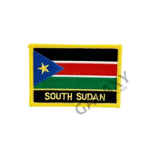 May include: A yellow embroidered patch featuring the flag of South Sudan. The flag depicts a black triangle with a gold star on a blue background, followed by horizontal red, white, and green stripes. The text "SOUTH SUDAN" is embroidered in gold beneath the flag.