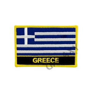 May include: Embroidered patch featuring the flag of Greece. The design includes blue and white stripes with a white cross in the upper left corner. The word "GREECE" is displayed in yellow letters on a black banner.