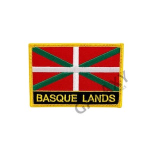 Peut inclure: Un écusson brodé avec le drapeau du Pays basque et le texte "BASQUE LANDS" en lettres dorées sur fond noir. L'écusson a une bordure jaune.