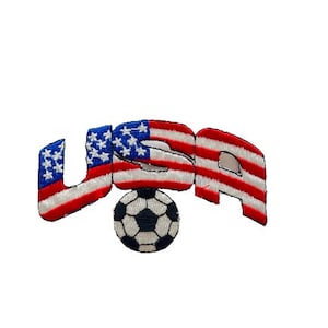 May include: Embroidered patch featuring the word "USA" with each letter designed as the American flag. A black and white soccer ball is positioned below the letters. The patch is likely for apparel or accessories.