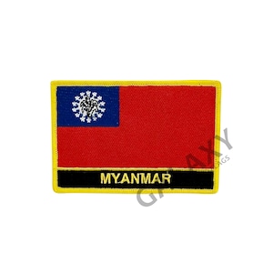 Op de afbeelding: Een rechthoekige patch met de vlag van Myanmar. De vlag heeft een rood veld met een blauw kanton met een wit embleem. Onder de vlag staat een zwarte balk met het woord "MYANMAR" in gouden letters, geel omlijnd.