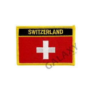 Puede incluir: Un parche bordado rojo, blanco y negro con la palabra "SWITZERLAND" en letras negras sobre fondo negro. El parche presenta la bandera suiza, una cruz blanca sobre fondo rojo, con un borde amarillo.
