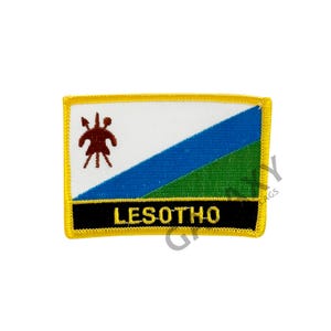 Könnte beinhalten: Gestickter Aufnäher mit der Flagge von Lesotho. Das Design umfasst einen weißen oberen Bereich, einen blauen diagonalen Streifen und einen grünen unteren Bereich. Das Wort "LESOTHO" wird in gelber Schrift auf einem schwarzen Banner angezeigt.
