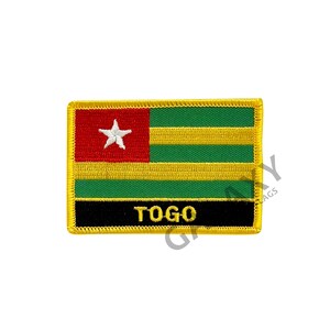 Puede incluir: Un parche bordado con la bandera de Togo. La bandera es roja, amarilla y verde con una estrella blanca en el cantón rojo. El parche tiene un borde negro con la palabra "TOGO" en letras amarillas.