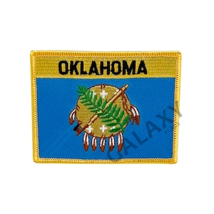 May include: An embroidered patch featuring the state flag of Oklahoma. The patch is rectangular and has a gold border. The flag depicts a blue background with a Native American symbol in the center. The symbol is a shield with a peace pipe and feathers. The word "OKLAHOMA" is written in black letters across the top of the patch.