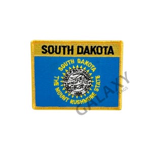 Könnte beinhalten: Ein gestickter Aufnäher in Gelb und Blau mit den Worten "SOUTH DAKOTA" in schwarzer Schrift. Der Aufnäher zeigt das Staatssiegel von South Dakota, das eine Darstellung der Landschaft des Staates und die Worte "THE MOUNT RUSHMORE STATE" enthält.