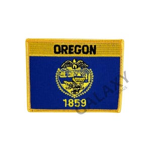 Puede incluir: Parche bordado con la bandera del estado de Oregón. El parche tiene un fondo azul con el sello del estado y el texto "OREGON" y "1859" en dorado. El borde es dorado.
