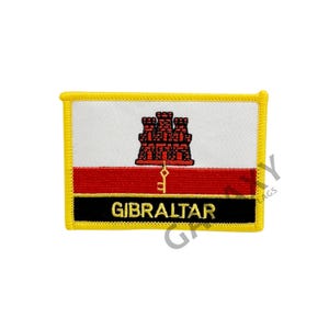 May include: Embroidered patch featuring the flag of Gibraltar. The design includes a white field, a red stripe, and a black band with the word "GIBRALTAR" in gold. The patch has a yellow border and a castle emblem.