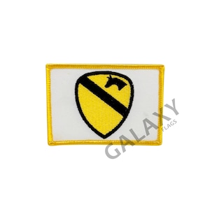 May include: A white patch with a yellow border and a yellow shield with a black silhouette of a horse's head. The shield has a black diagonal stripe across it. The patch is embroidered.