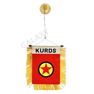 Puede incluir: Una pequeña bandera roja con una estrella amarilla en un círculo negro. La bandera tiene la palabra "KURDS" impresa y está colgada de una cuerda blanca.