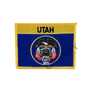 Puede incluir: Un parche bordado en oro con el sello del estado de Utah. El sello presenta un águila calva, una colmena y las palabras "Industry" y "Utah 1847 1896". El parche tiene un borde dorado y la palabra "Utah" en letras negras en la parte superior.