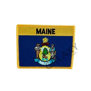 May include: An embroidered patch featuring the state seal of Maine, with a blue background and gold border. The word "MAINE" is embroidered in black lettering.
