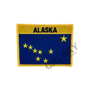 May include: A blue and gold embroidered patch with the word "ALASKA" and a yellow star in the upper right corner. The patch features a constellation of eight yellow stars in the shape of the Big Dipper.