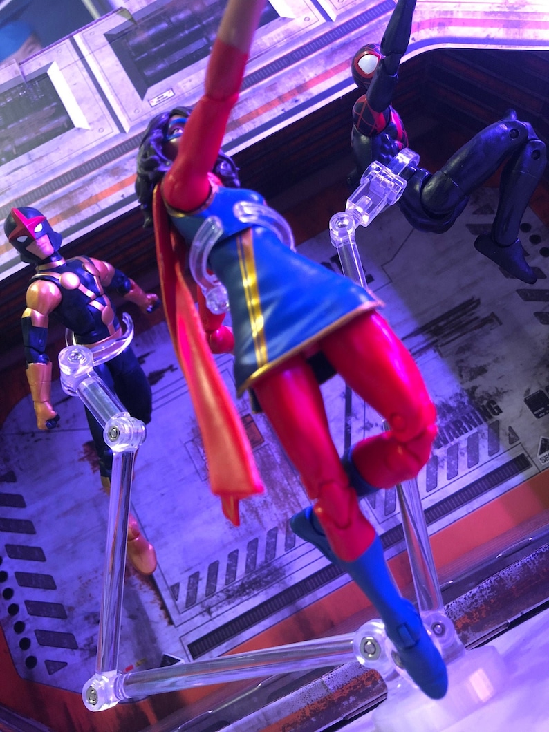 May include: Three action figures, a red, blue, and gold superhero, a black superhero with red accents, and a black superhero with red and blue accents. The figures are posed on clear plastic stands.