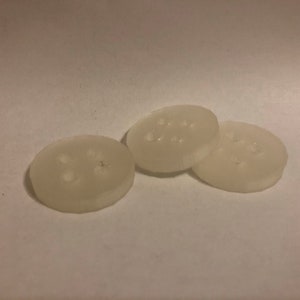 May include: Three white plastic buttons with multiple holes. The buttons are round and have a slightly raised edge.