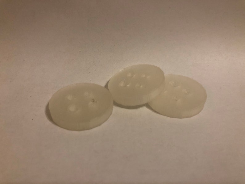 May include: Three white plastic buttons with multiple holes. The buttons are round and have a slightly raised edge.