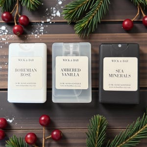 May include: Three rectangular hand sanitizer spray bottles. One is white, one is clear, and one is black. Each has a label that reads "WICK & BAR" and a scent name: "Bohemian Rose", "Ambered Vanilla", and "Sea Minerals". The bottles are 20 ml.