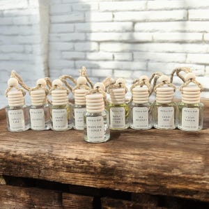 May include: Ten small glass bottles with wooden caps and string hangers. Each bottle contains a car diffuser with a different scent. The scents are Vanilla Cake, Lavender, Coffee House, Apple Honey, White Oak & Vanilla, Mango & Coconut Milk, Sea Minerals, Ocean Rose, and Clean Cotton.