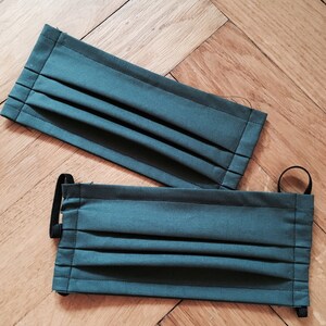 May include: Two dark green fabric face masks with pleats and black elastic ear loops.