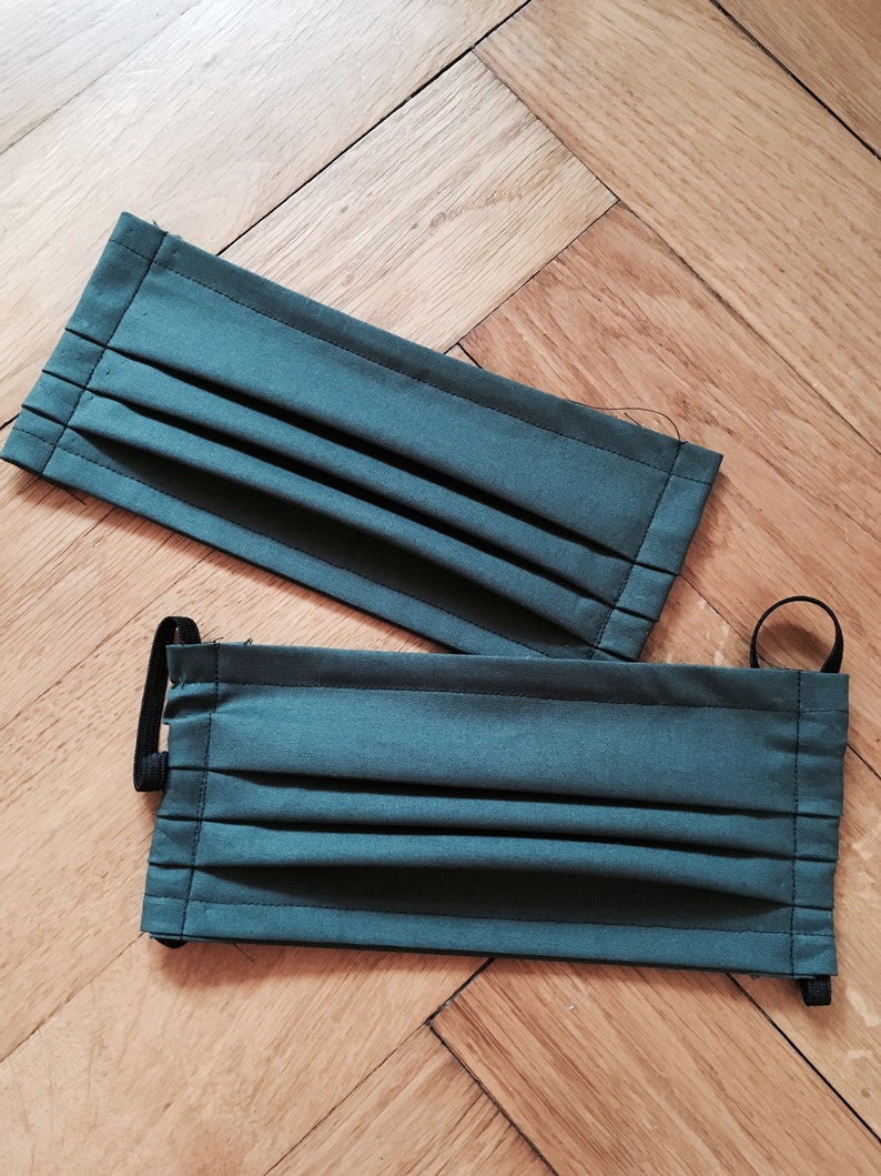 May include: Two dark green fabric face masks with pleats and black elastic ear loops.