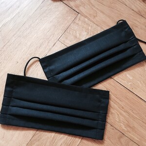 May include: Two pleated fabric face masks, one black and one dark green, laid out on a wooden surface.